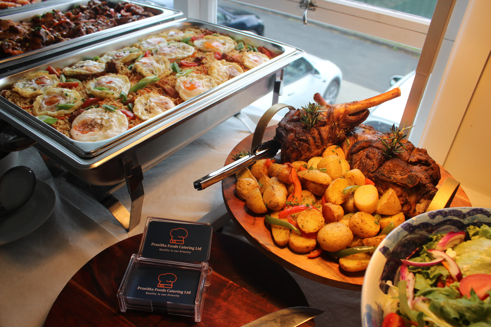 Buffet display with egg fried rice chafing dish, roast lamb leg on potatoes and Pranitha Foods branded business cards